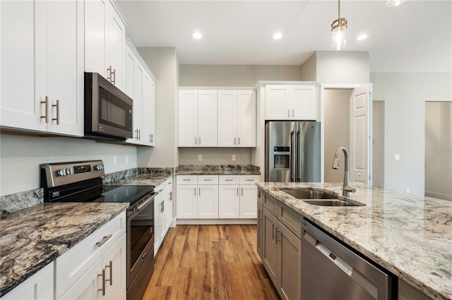 kitchen with light wood finished floors, appliances with stainless steel finishes, hanging light fixtures, white cabinets, and a sink