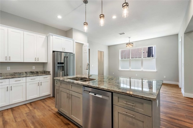 kitchen with decorative light fixtures, an island with sink, appliances with stainless steel finishes, wood finished floors, and a sink