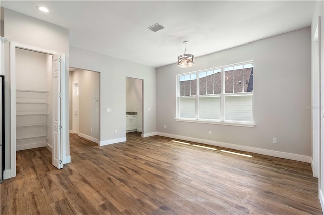 unfurnished bedroom featuring a spacious closet, visible vents, baseboards, and wood finished floors