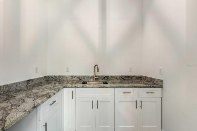 kitchen with white cabinets, light stone countertops, and a sink