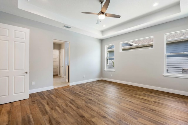 empty room featuring visible vents, baseboards, a tray ceiling, wood finished floors, and a ceiling fan