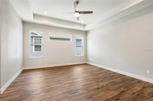 empty room featuring a raised ceiling, recessed lighting, wood finished floors, and baseboards