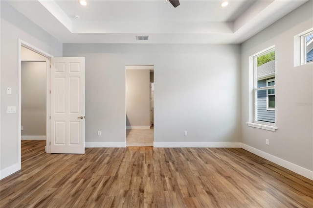 interior space featuring visible vents, baseboards, a tray ceiling, and wood finished floors