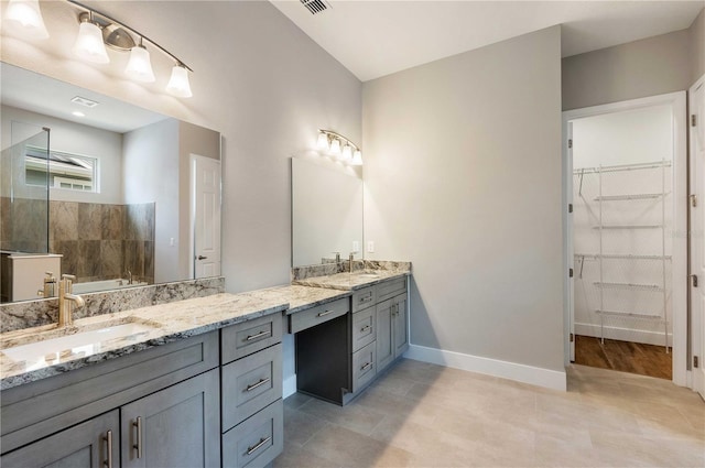 bathroom with vanity, visible vents, baseboards, a tile shower, and a walk in closet