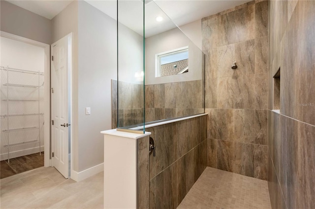 full bath with a spacious closet, a walk in shower, baseboards, and wood finished floors