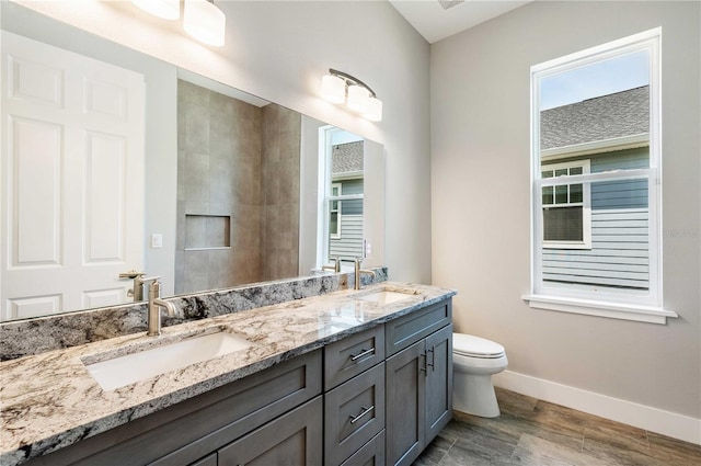 bathroom featuring double vanity, toilet, baseboards, and a sink