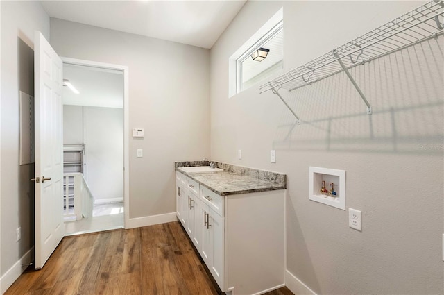 washroom with hookup for a washing machine, wood finished floors, baseboards, cabinet space, and a sink