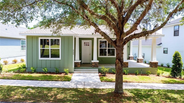 view of front facade featuring a porch, board and batten siding, roof with shingles, and a front lawn