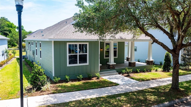 view of front of house with a porch, board and batten siding, a front yard, and roof with shingles