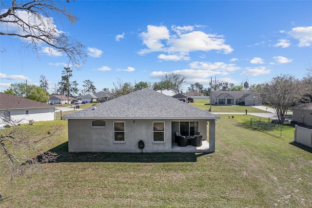 view of side of property featuring stucco siding, fence, a yard, a residential view, and a shingled roof