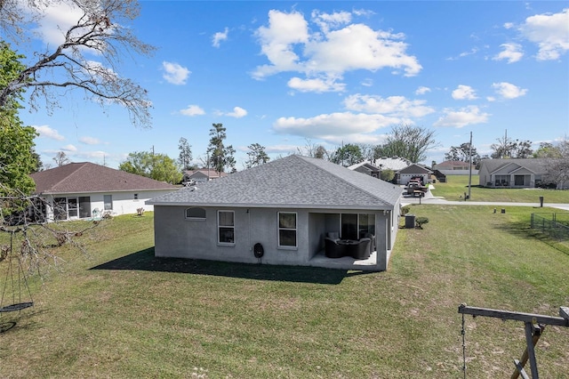 rear view of house featuring stucco siding, a lawn, and roof with shingles