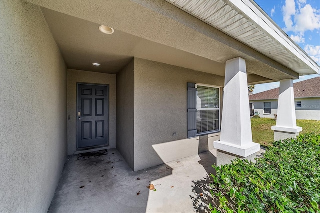 view of exterior entry with stucco siding and a porch