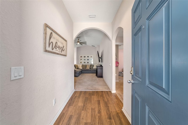 corridor featuring visible vents, dark wood-type flooring, baseboards, vaulted ceiling, and arched walkways