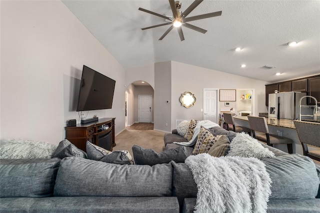 living area featuring a ceiling fan, baseboards, arched walkways, vaulted ceiling, and light colored carpet