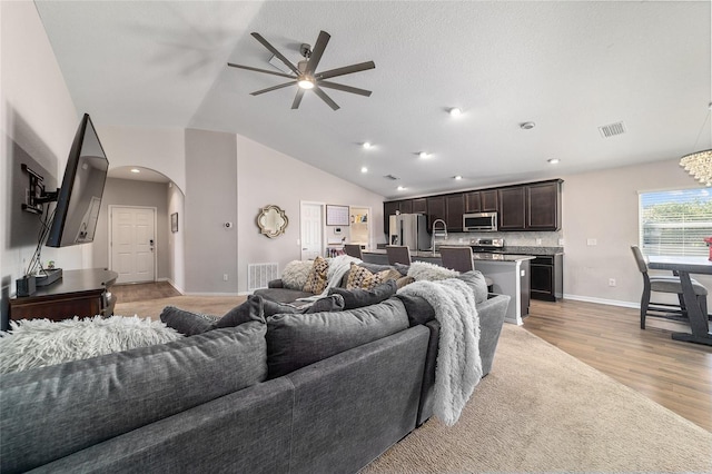 living area featuring visible vents, lofted ceiling, arched walkways, light wood finished floors, and baseboards