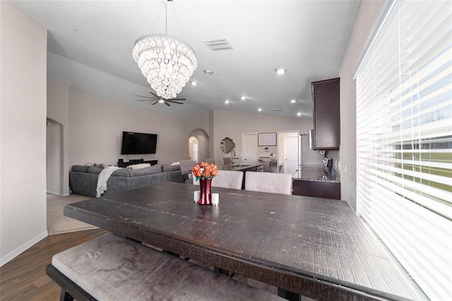 dining area featuring wood finished floors, visible vents, arched walkways, vaulted ceiling, and a notable chandelier