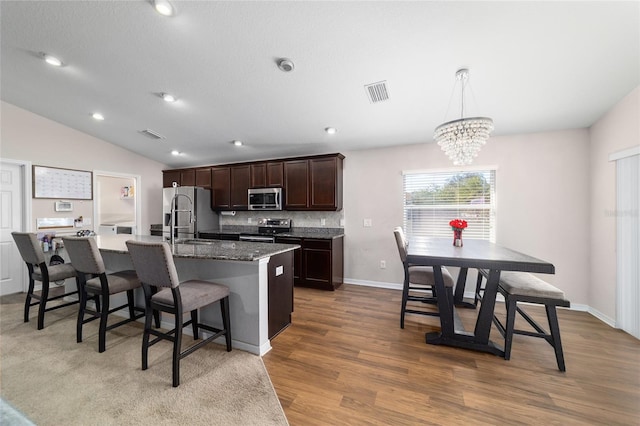 kitchen featuring visible vents, a kitchen island with sink, stainless steel appliances, dark brown cabinets, and vaulted ceiling