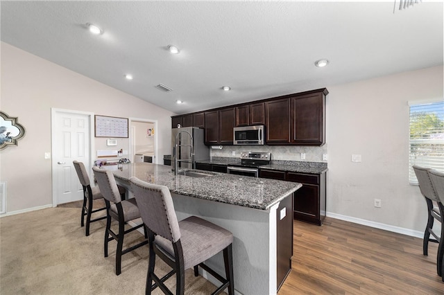 kitchen with a sink, a kitchen breakfast bar, stainless steel appliances, lofted ceiling, and dark brown cabinets