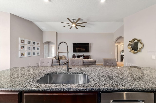 kitchen with open floor plan, dark stone counters, vaulted ceiling, arched walkways, and a sink