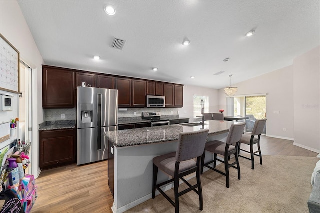 kitchen with tasteful backsplash, an island with sink, vaulted ceiling, a kitchen breakfast bar, and stainless steel appliances