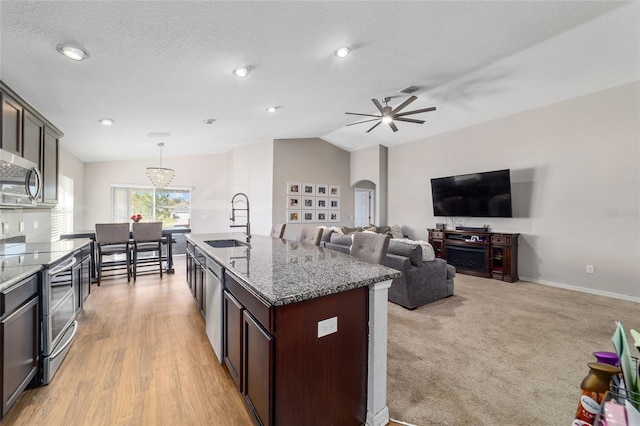 kitchen with arched walkways, stainless steel appliances, a sink, dark brown cabinetry, and vaulted ceiling