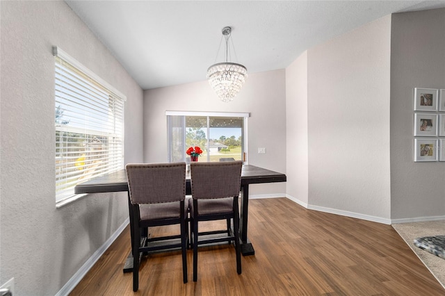 dining space featuring baseboards, a notable chandelier, wood finished floors, and vaulted ceiling