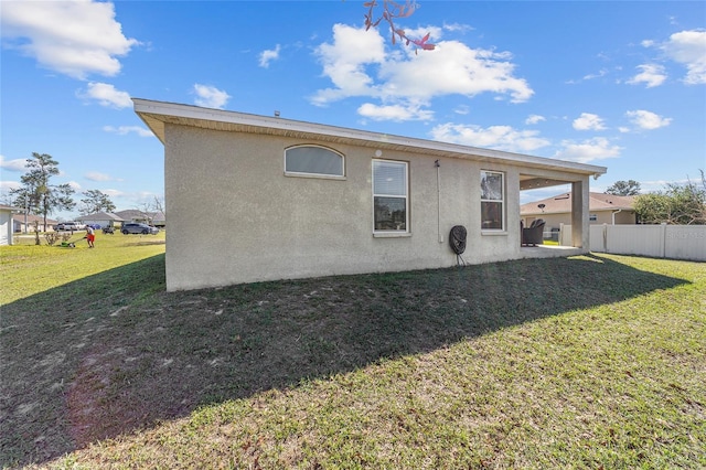 back of house featuring stucco siding, a yard, and fence