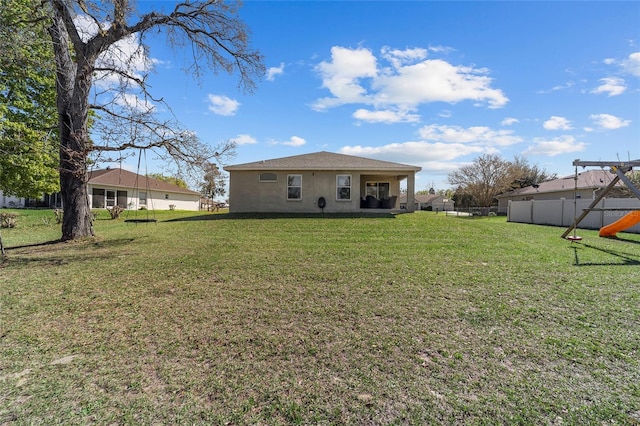 rear view of house featuring stucco siding, a lawn, a playground, and fence