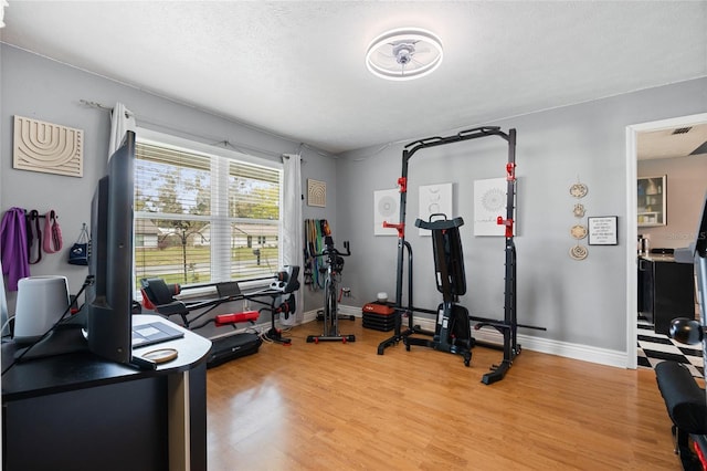 exercise area with visible vents, baseboards, a textured ceiling, and light wood-style flooring