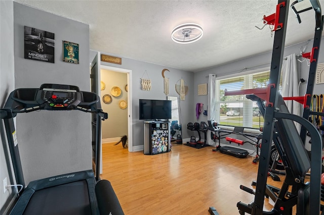 workout area with baseboards, a textured ceiling, and light wood-style flooring