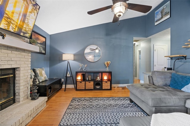 living area with baseboards, a brick fireplace, wood finished floors, and vaulted ceiling