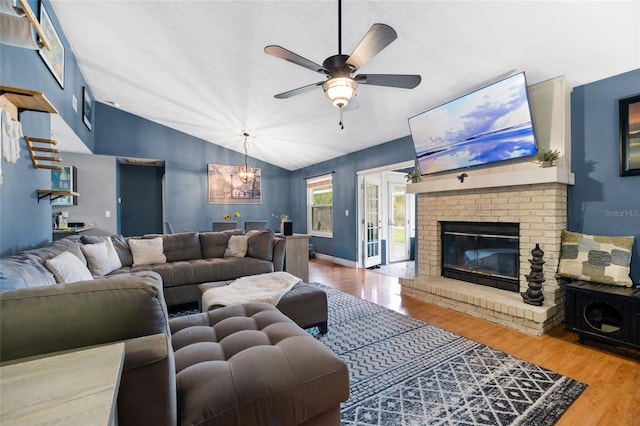 living room featuring lofted ceiling, wood finished floors, baseboards, a brick fireplace, and ceiling fan