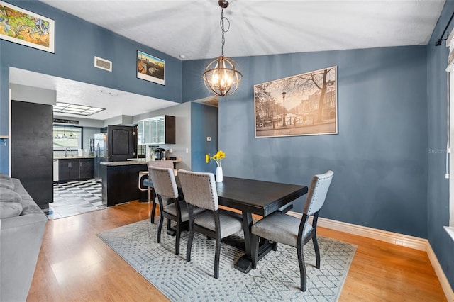 dining space with light wood finished floors, visible vents, baseboards, and an inviting chandelier