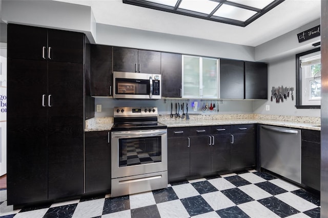 kitchen featuring dark cabinetry, light floors, light stone countertops, and stainless steel appliances