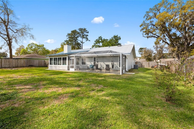 rear view of property featuring a lawn, a fenced backyard, a chimney, and a sunroom