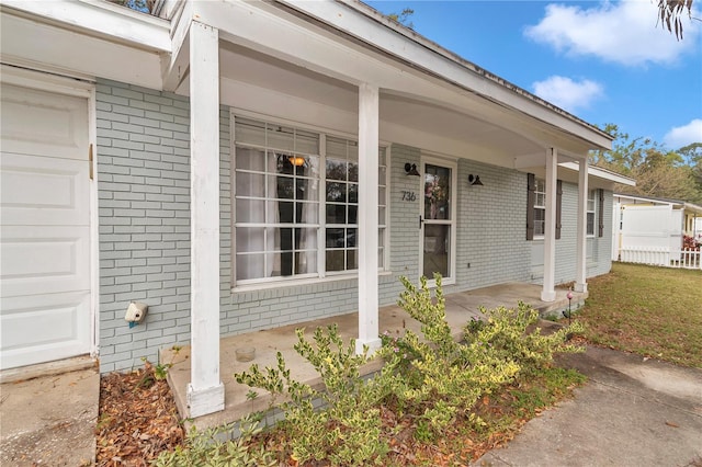 entrance to property with brick siding, covered porch, and an attached garage