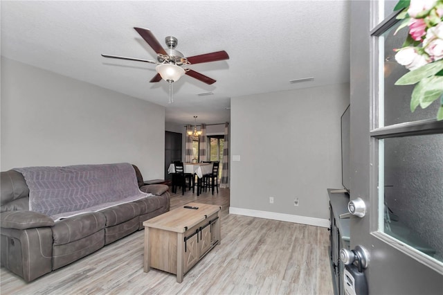 living area with visible vents, baseboards, light wood-style flooring, ceiling fan with notable chandelier, and a textured ceiling