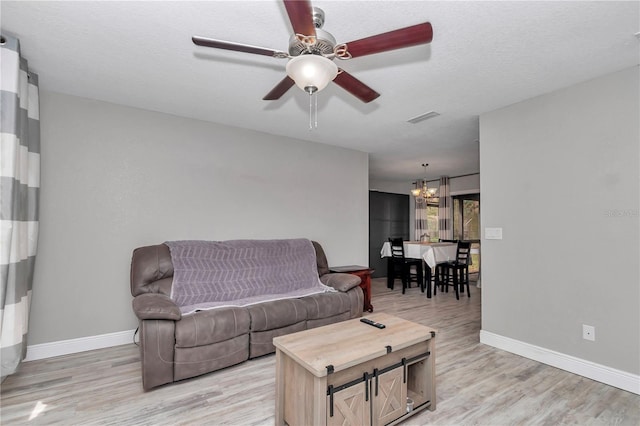 living area with ceiling fan with notable chandelier, light wood-style flooring, baseboards, and visible vents