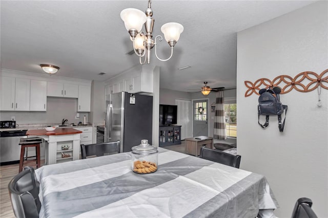 dining space featuring light wood-type flooring, a textured ceiling, and ceiling fan with notable chandelier