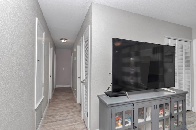 corridor with light wood-type flooring, baseboards, a textured ceiling, and a textured wall