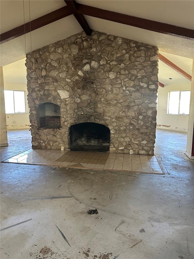 unfurnished living room featuring a stone fireplace, plenty of natural light, and lofted ceiling with beams