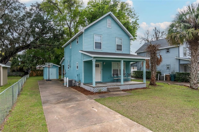 view of front of home with a shed, fence, covered porch, a front yard, and central AC unit