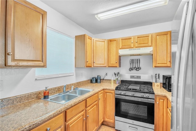 kitchen with under cabinet range hood, a sink, freestanding refrigerator, light countertops, and stainless steel gas range