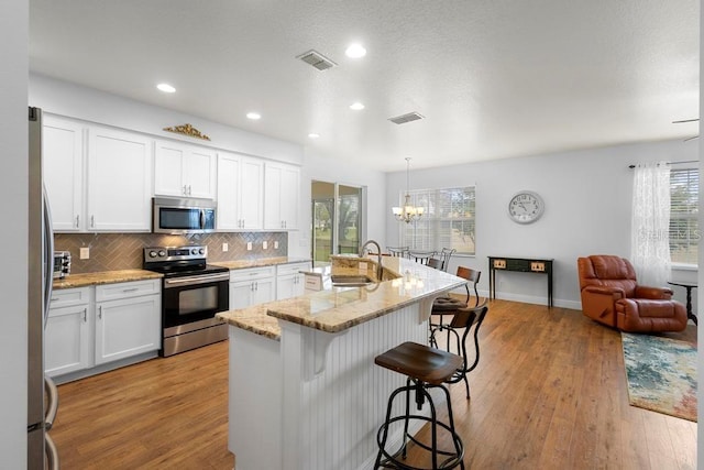 kitchen featuring a sink, decorative backsplash, appliances with stainless steel finishes, a kitchen breakfast bar, and light wood-type flooring