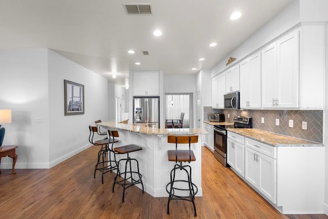 kitchen featuring tasteful backsplash, visible vents, a kitchen breakfast bar, white cabinets, and stainless steel appliances