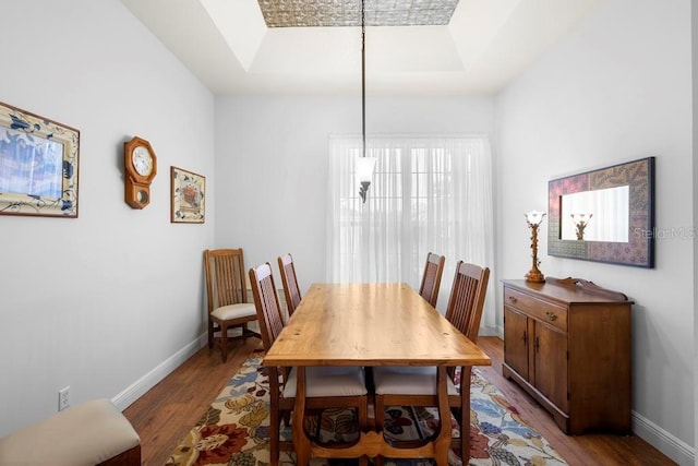 dining room with a raised ceiling, baseboards, and wood finished floors