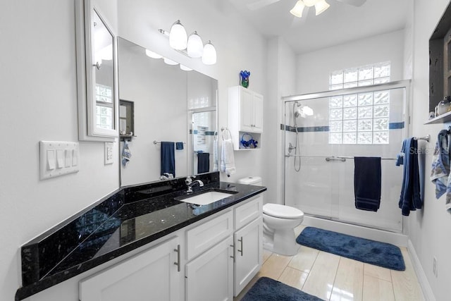 bathroom featuring wood tiled floor, toilet, a stall shower, vanity, and a ceiling fan