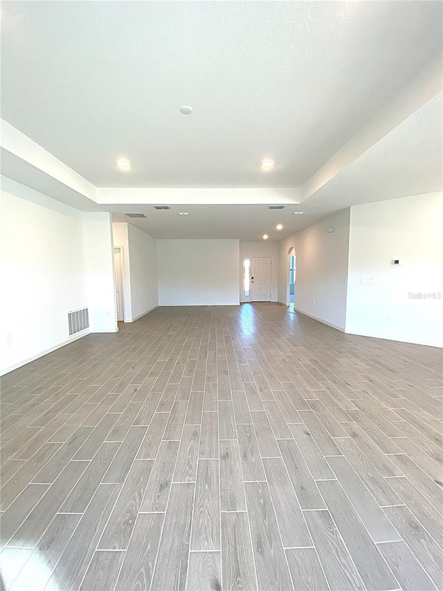 empty room with visible vents, recessed lighting, a raised ceiling, and wood finish floors