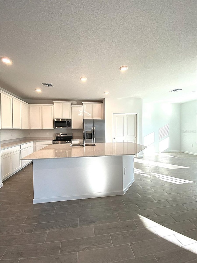 kitchen featuring visible vents, an island with sink, white cabinetry, appliances with stainless steel finishes, and wood tiled floor