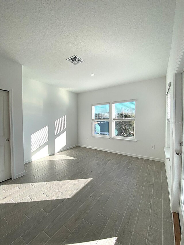 empty room featuring baseboards, visible vents, a textured ceiling, and wood finish floors